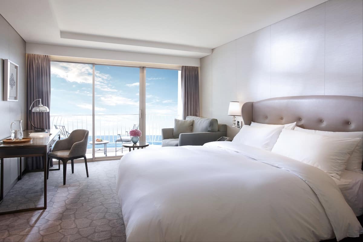 Quarto de hotel com uma cama grande, uma escrivaninha, uma cadeira e vista para o oceano.