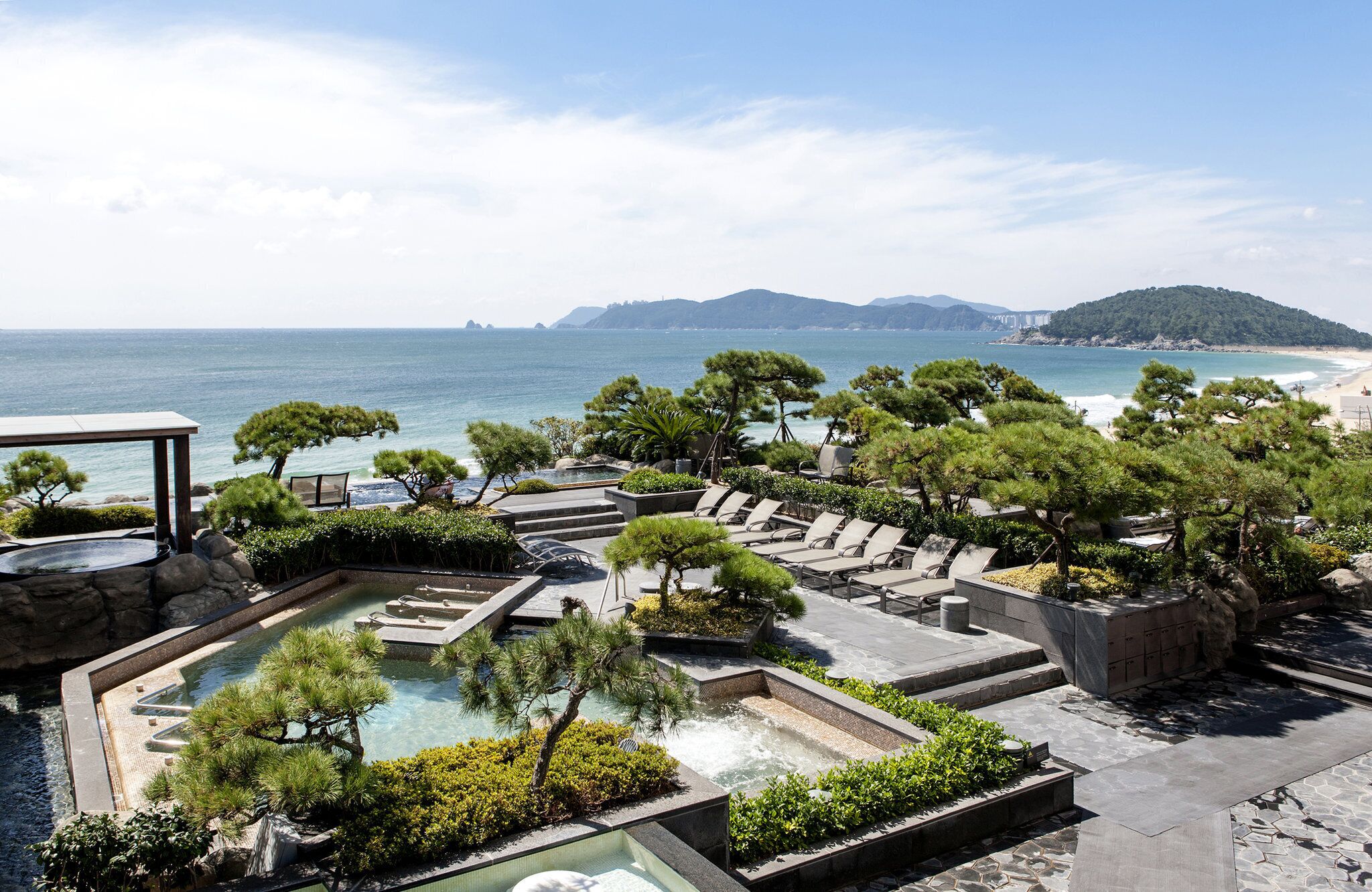 Un resort con piscina, sillones de descanso y vistas al mar y las montañas.