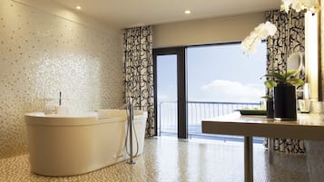 A modern bathroom with a bathtub, a shower, and a vanity with a mirror. There is a balcony with a railing and a view of the sky.