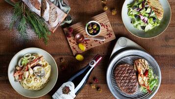 Una mesa de madera con una variedad de platos, como pasta con mariscos, un bistec a la parrilla y una ensalada, además de pan y una botella de vino.