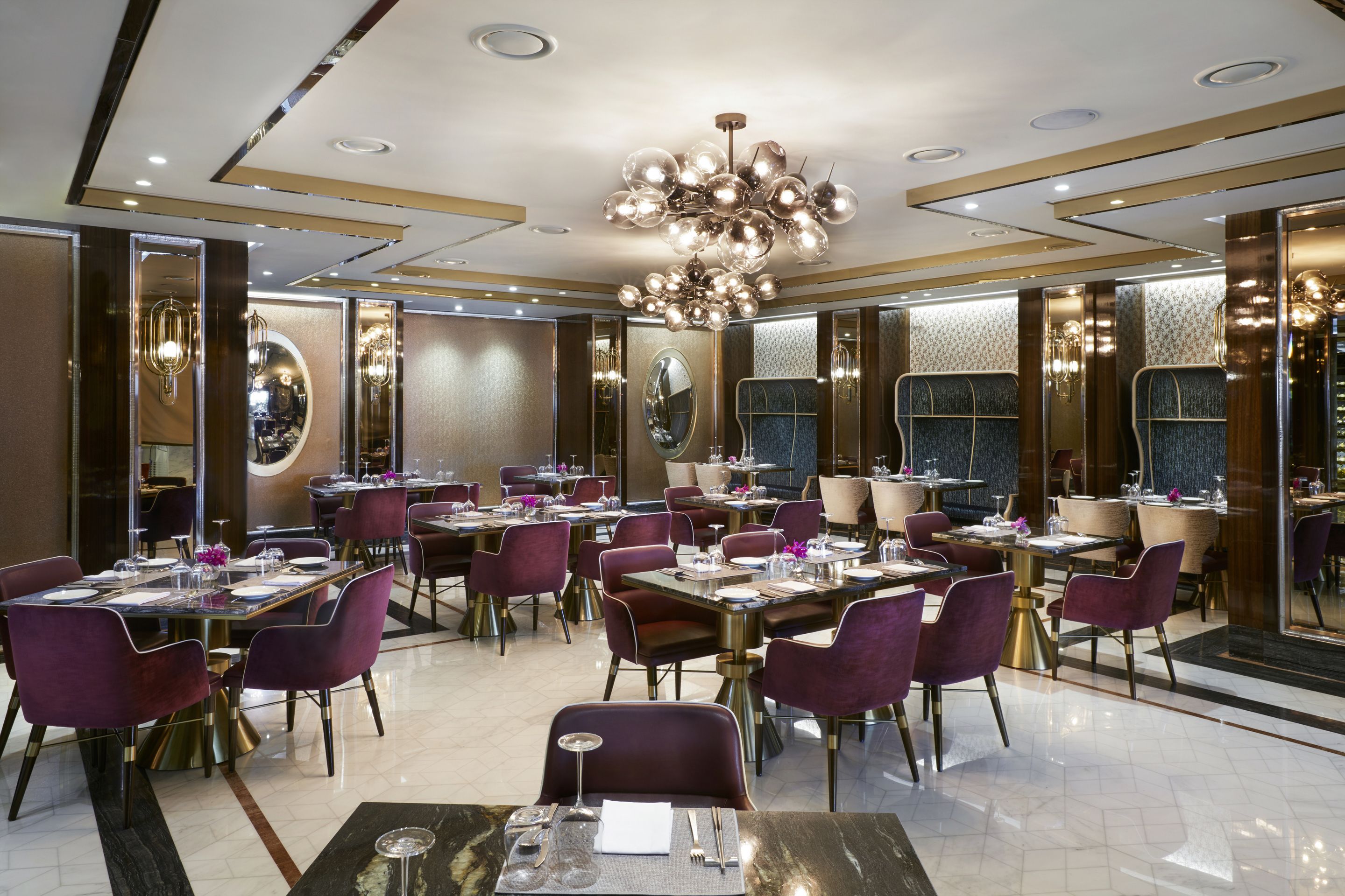 A modern restaurant with round tables, purple chairs, and a chandelier.