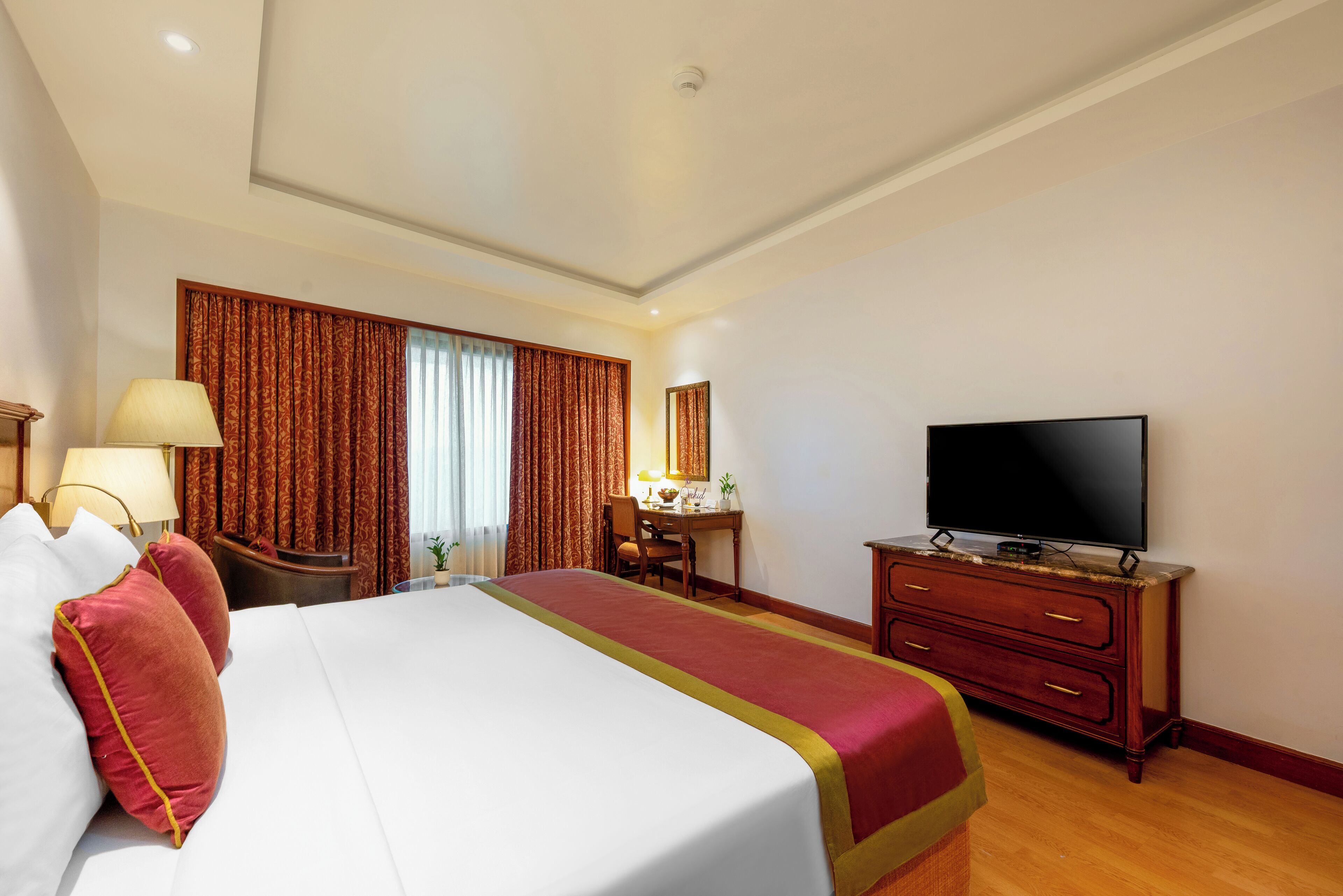 Quarto de hotel com uma cama grande, uma escrivaninha, uma televisão e um armário.