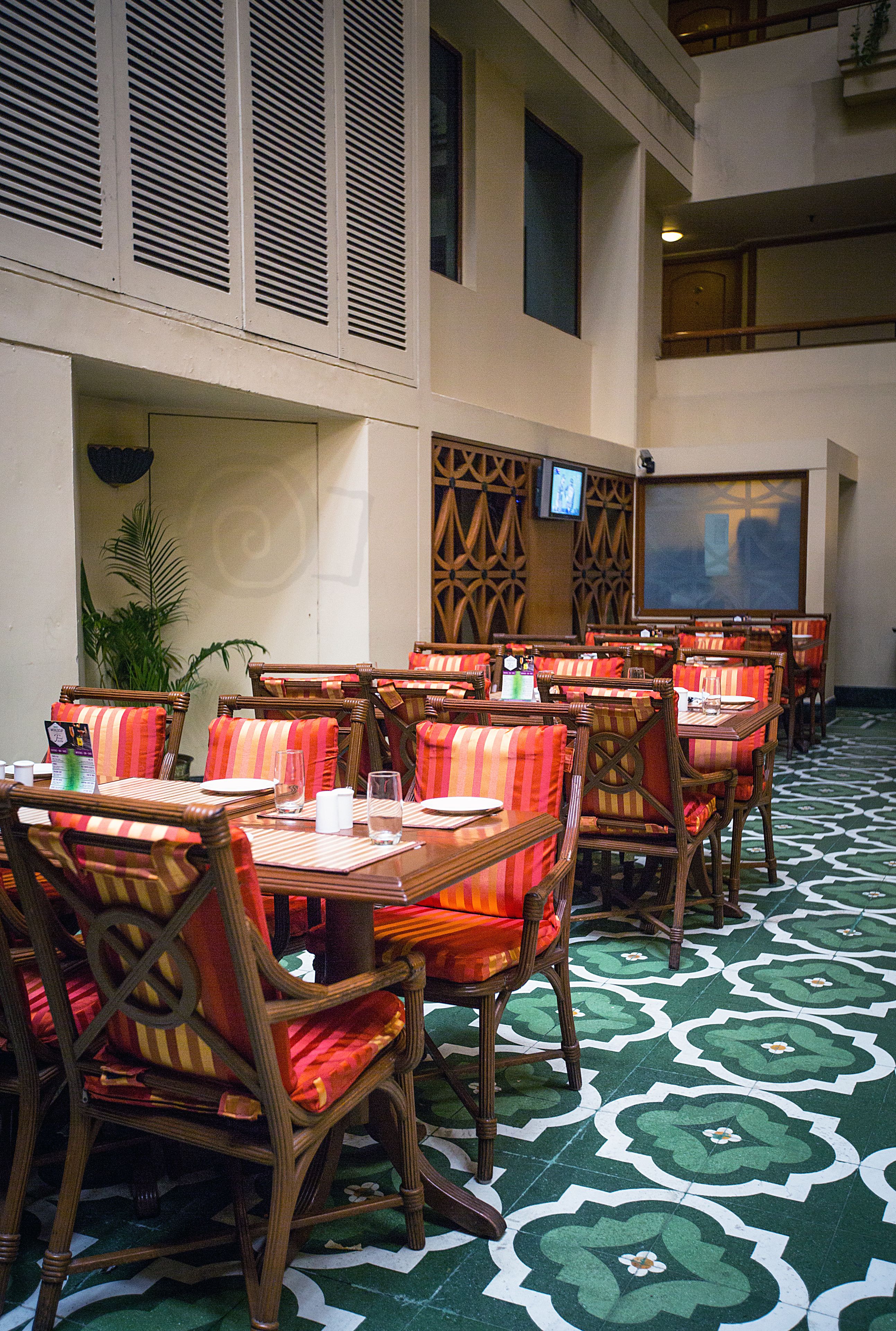 A restaurant with multiple tables and chairs, a patterned floor, and a television screen on the wall.
