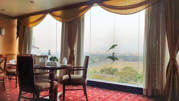 A dining area with a table set for two, large windows with curtains, and a view of a cityscape.