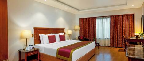 A hotel room with a large bed, two bedside tables with lamps, a desk, and a chair.