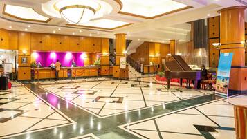 Un hall de hotel con mostrador de recepción, un piano de cola, una escalera y un piso con diseño.