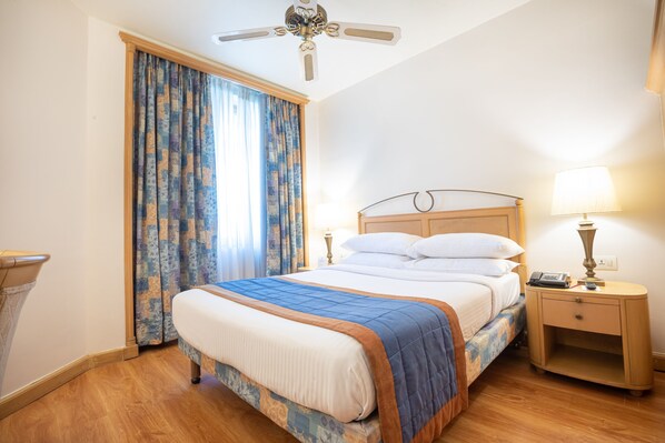 Una habitación de hotel con cama, mesita de noche, lámpara y ventilador de techo.