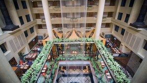 Ein mehrgeschossiges Atrium mit einem offenen zentralen Bereich, umgeben von Tischen und Stühlen, Balkonen mit Pflanzen und einer großen, hängenden Struktur.