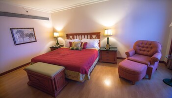 Un dormitorio ordenado con una cama grande, dos mesitas de noche con lámparas, una silla y una pequeña mesa.
