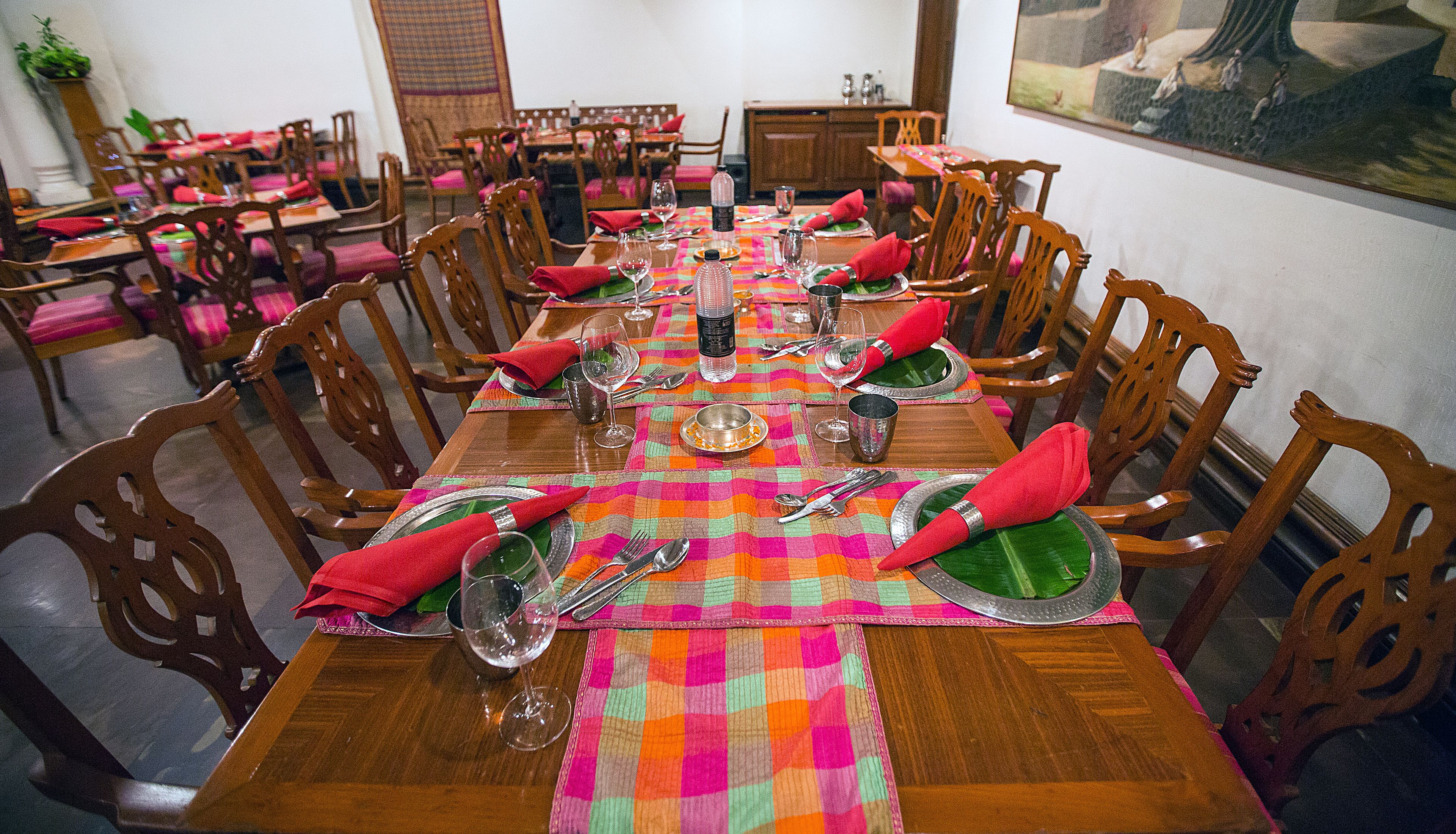 A dining area with wooden tables and chairs, each set with plates, cutlery, and glasses.