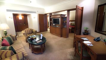 A hotel room with a living area featuring a sofa, a coffee table, a desk, and a television.