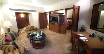 A hotel room with a living area featuring a sofa, a coffee table, a desk, and a television.