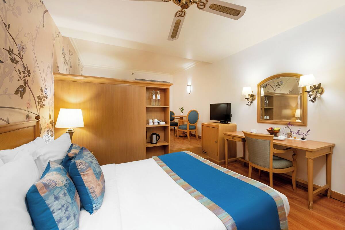 Een hotelkamer met een bed, bureau, stoel, televisie, kast en een spiegel.