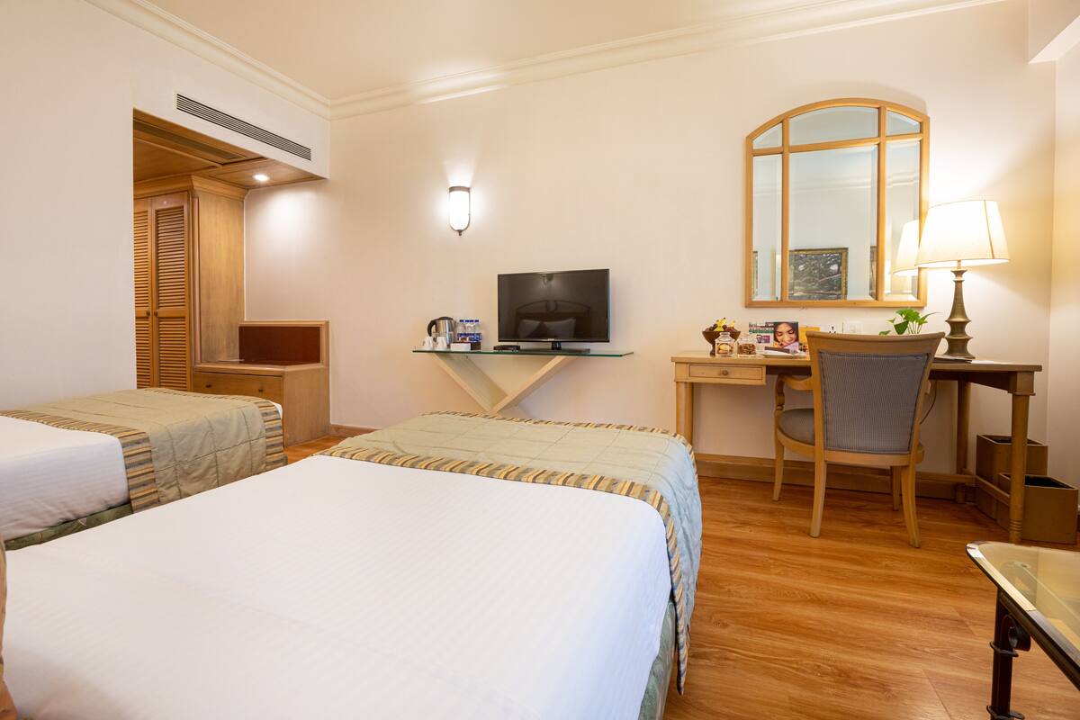 Een hotelkamer met twee bedden, een bureau met een computer, een stoel, een televisie en een spiegel.
