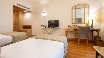 A hotel room with two beds, a desk with a computer, a chair, a TV, and a mirror.