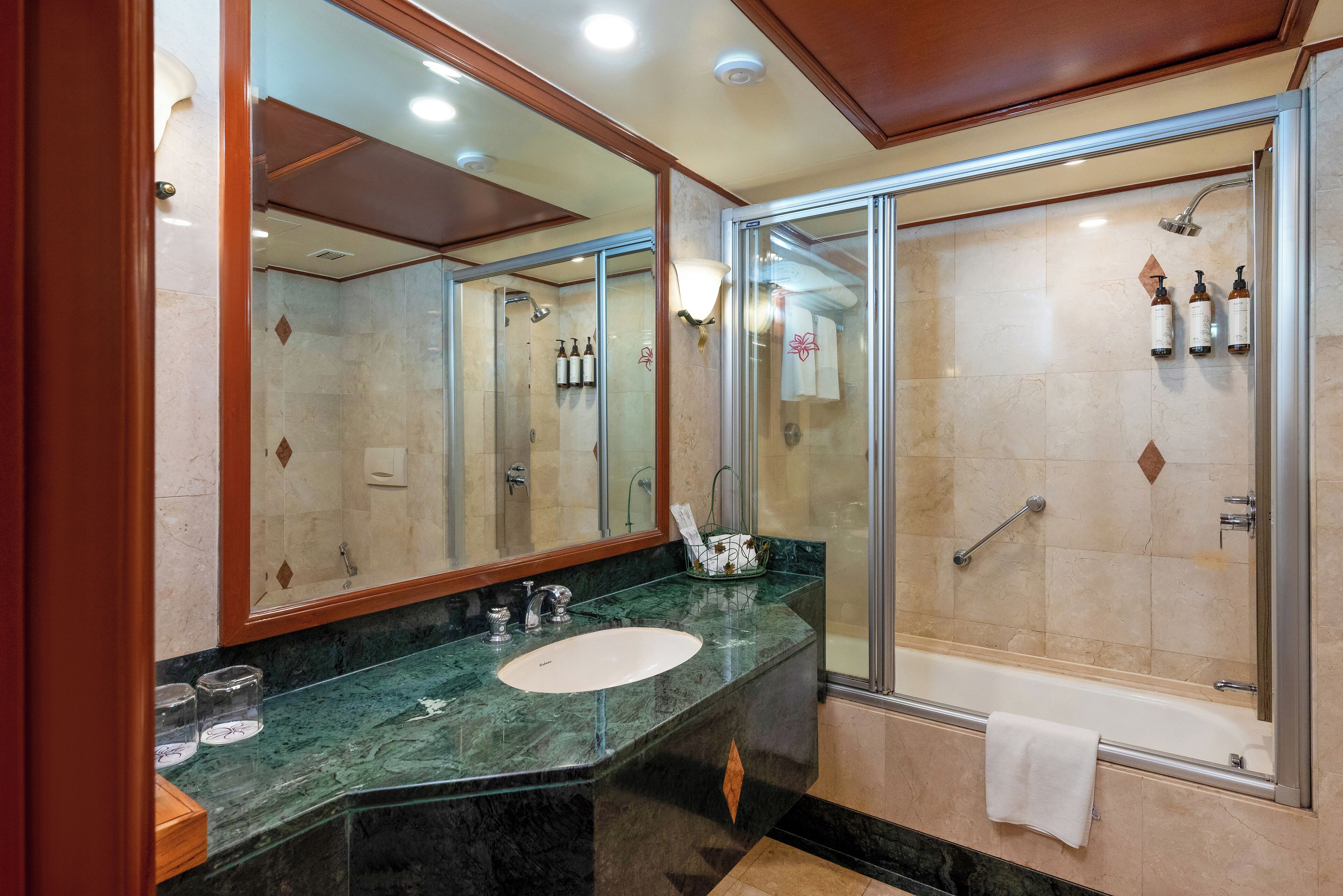 Un baño moderno con ducha de vidrio, lavamanos de mármol y un espejo grande.