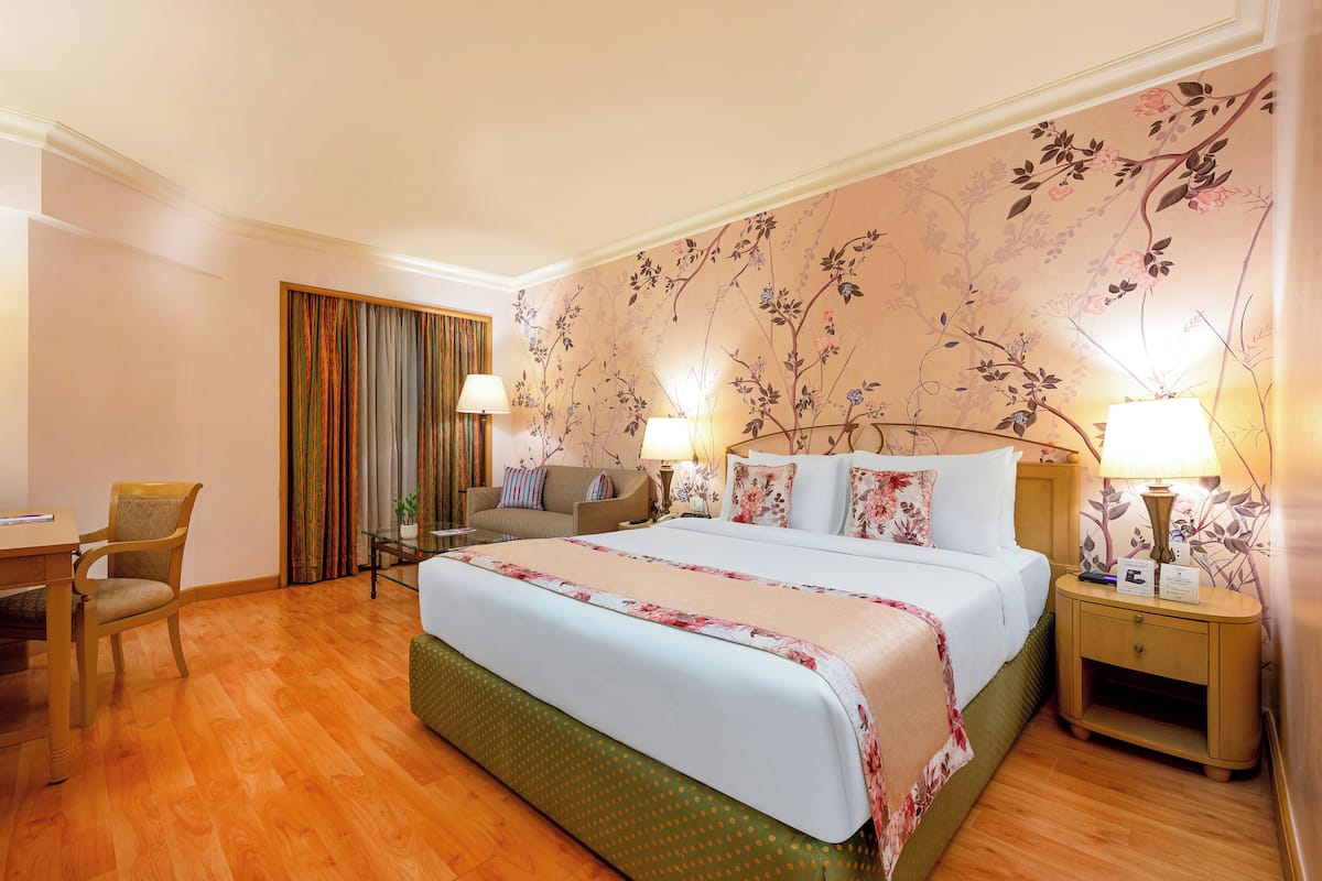 Een hotelkamer met een groot bed, een bureau, een stoel en een nachtkastje met lampen.