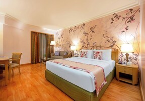 A hotel room with a large bed, a desk, a chair, and a nightstand with lamps.