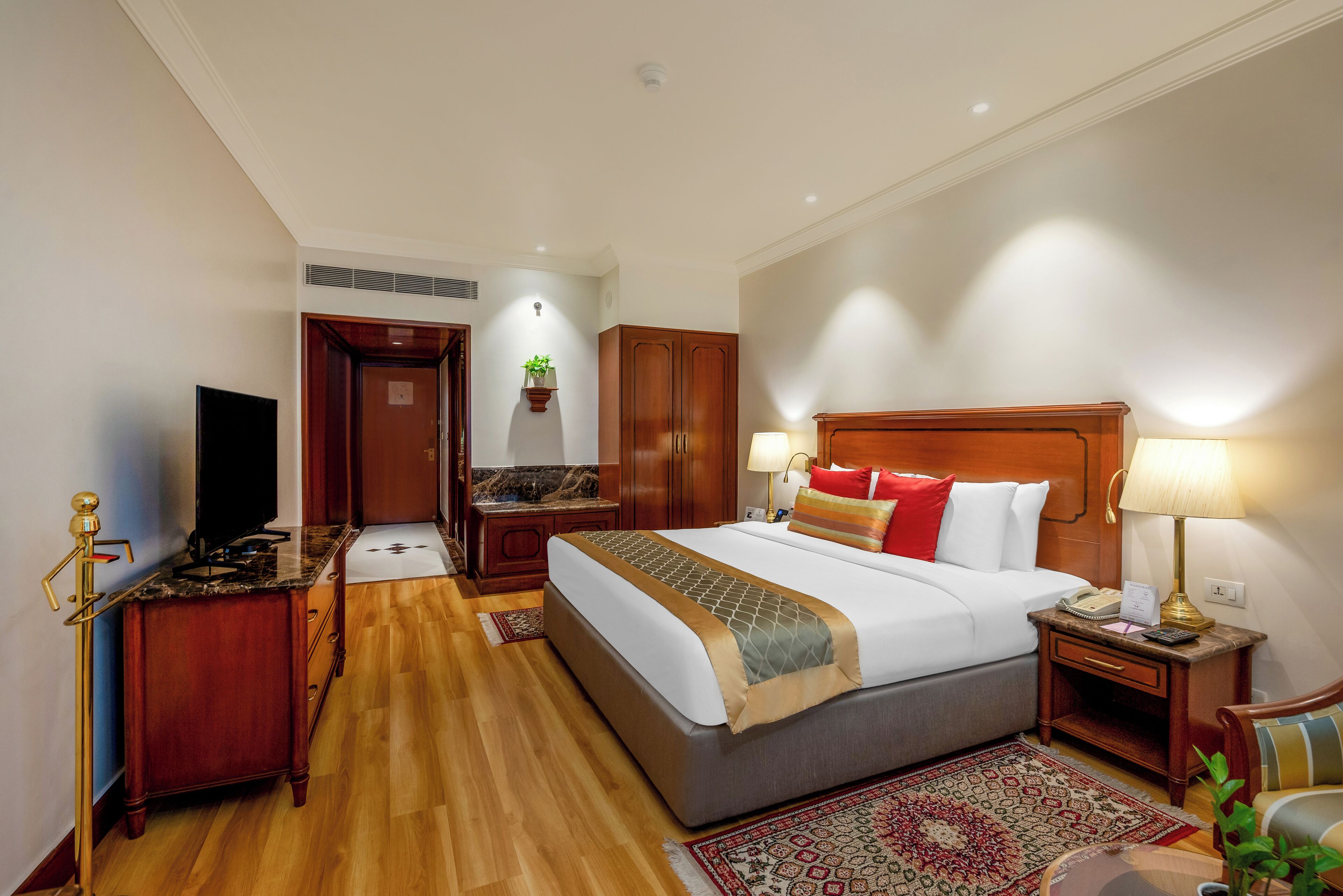 A hotel room with a large bed, wooden furniture, a television, and a desk.
