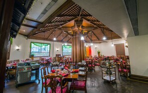 Een ruim restaurant met hoge houten plafonds, meerdere eettafels en een centraal gelegen keuken.
