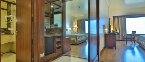 Una habitación de hotel con un espejo grande, muebles de madera, una cama, un escritorio y una silla.