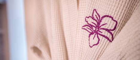 Ein Detailaufnahme eines beige farbenen, strukturierten Stoffes mit einer violett bestickten Blume.