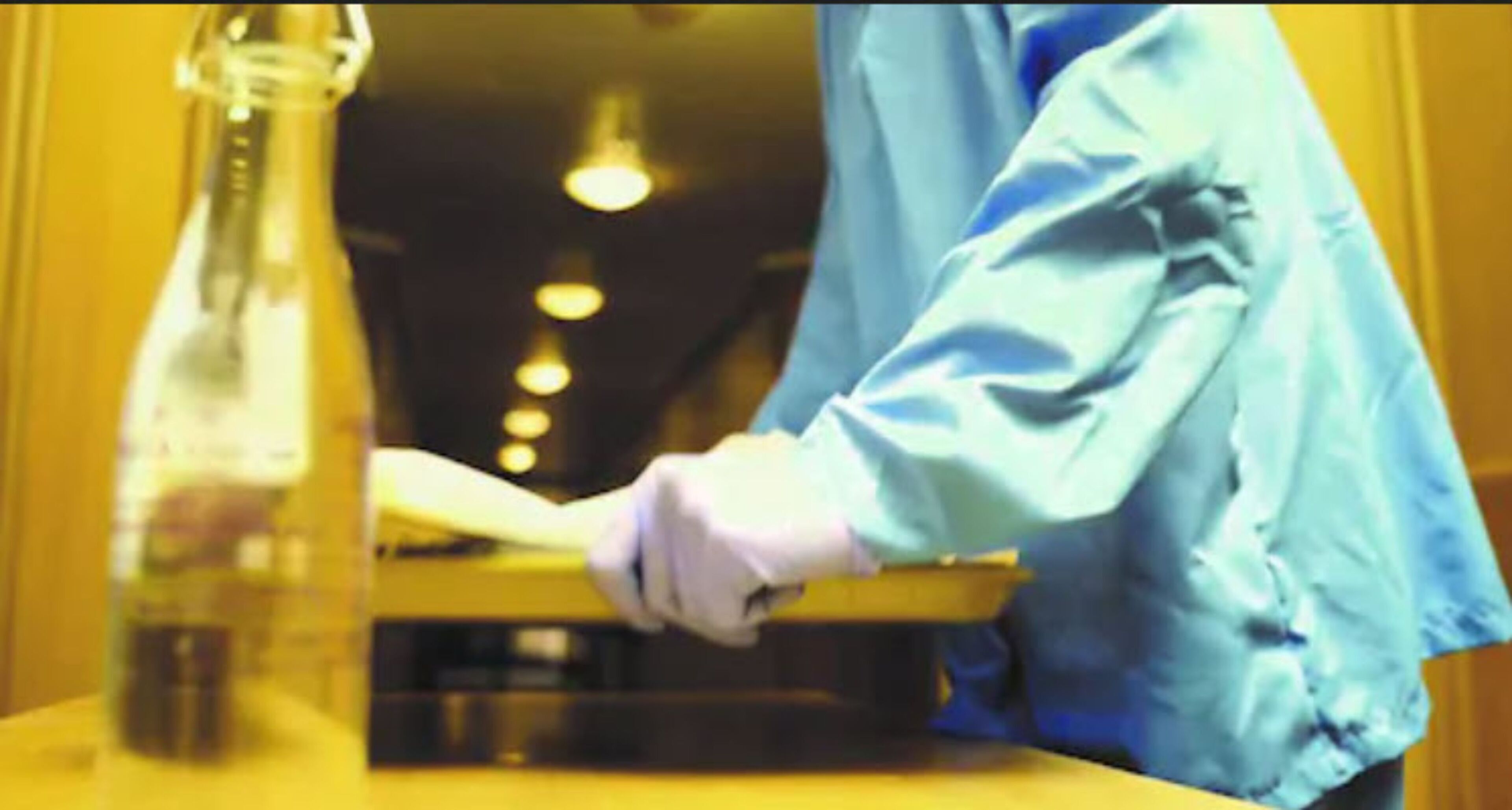 A person in a blue shirt and white gloves handling a glass container.