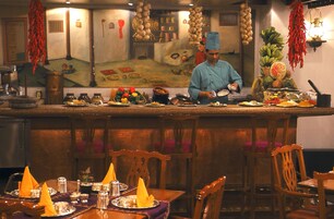 Een restaurant met een kok die eten bereidt aan de bar, houten stoelen en een tafel gedekt met borden en bestek.