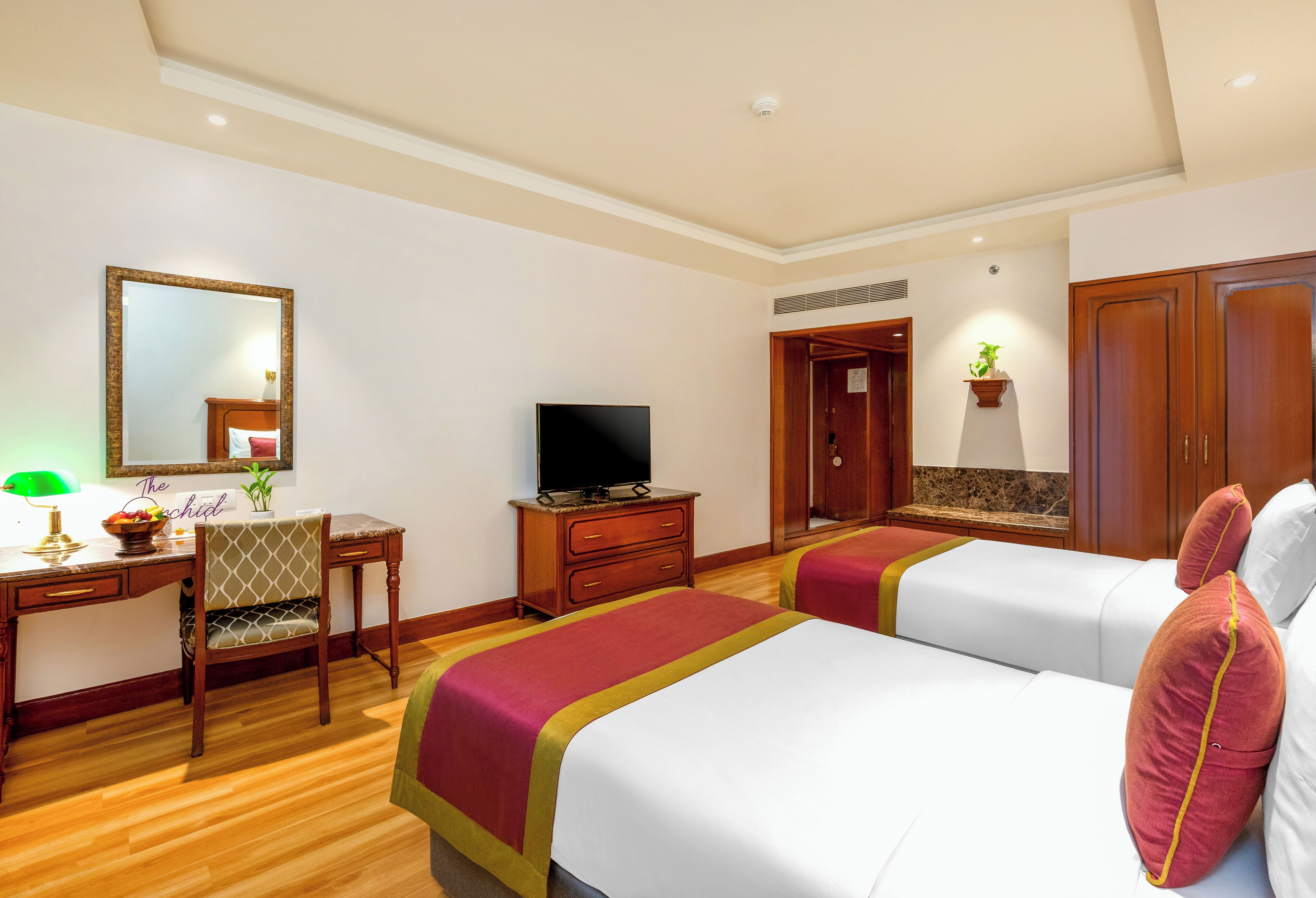 Ein Hotelzimmer mit zwei Betten, einem Schreibtisch mit Fernseher, einem Sessel und einem Spiegel.