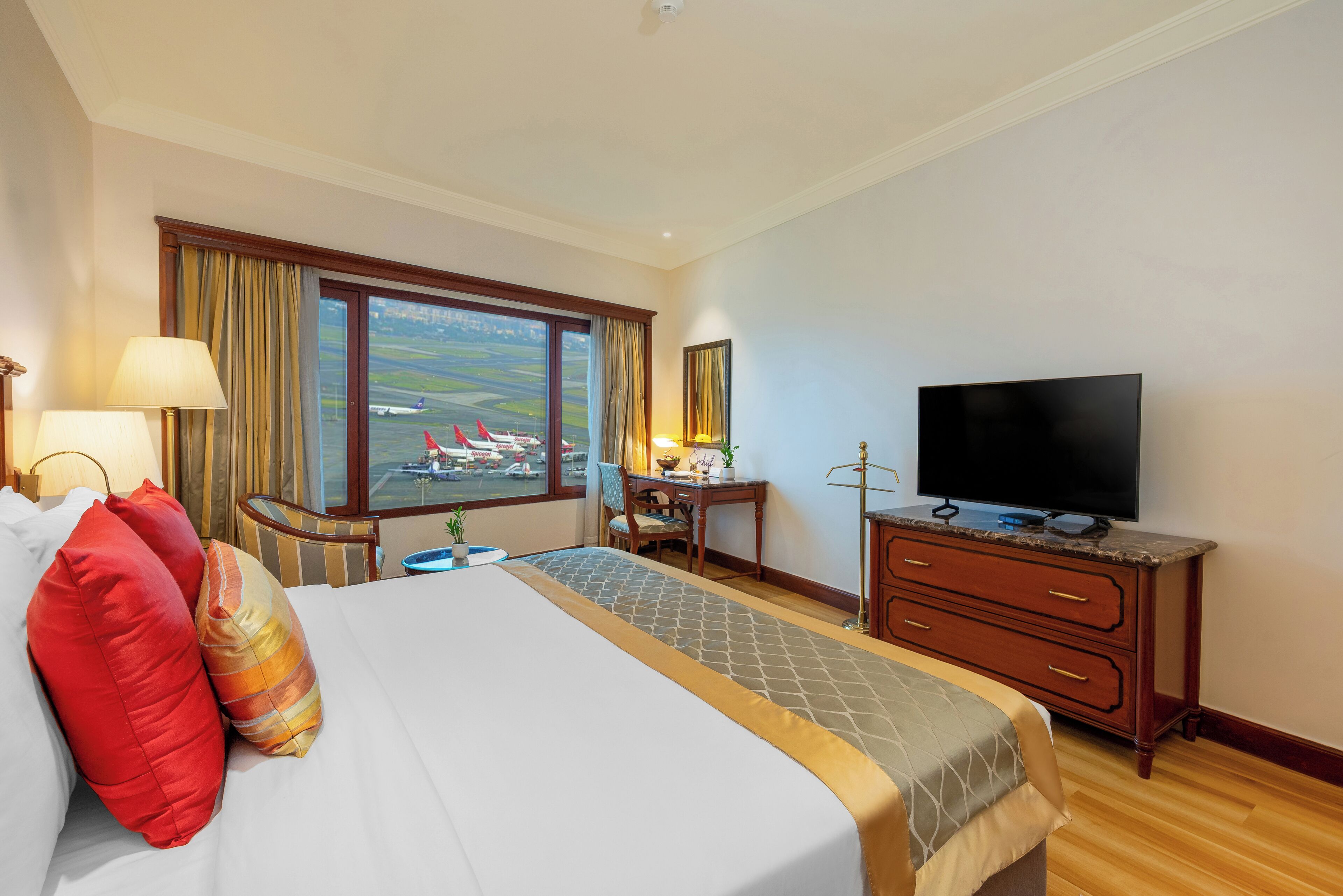 Habitación de hotel con una cama grande, un escritorio, un televisor y una ventana con vistas a aviones.