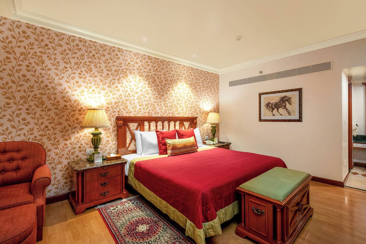 Een slaapkamer met een groot bed, twee nachtkastjes, een houten stoel, een tapij트 en een lijst met een afbeelding aan de muur.