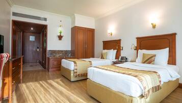 A hotel room with two beds, wooden headboards, a marble-topped dresser, a desk, and a television.