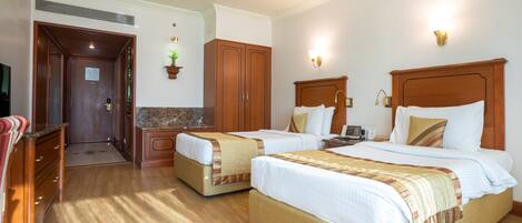 A hotel room with two beds, wooden headboards, a marble-topped dresser, a desk, and a television.