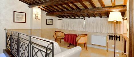 A room with a wooden ceiling, a cushioned bench, a table with chairs, a floor lamp, and a radiator.