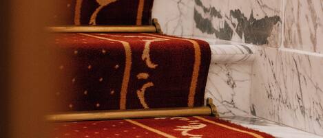 Een trap met treden bekleed met rood tapijt en muren van wit marmer.