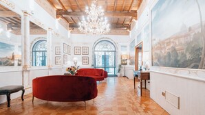 A spacious room with a large window, a chandelier, and a red sofa. - Hotel Pantheon (Rome)
