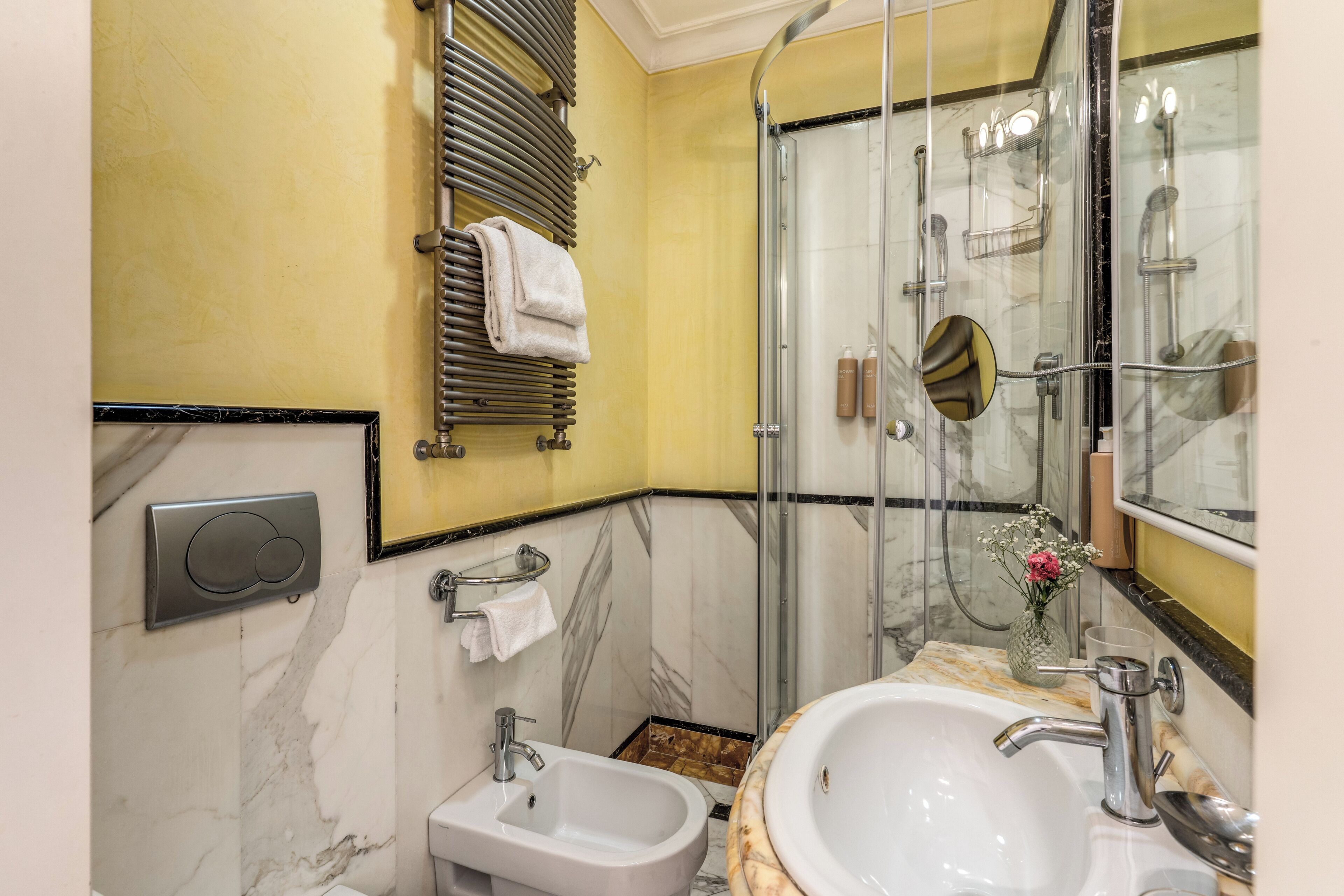 Un baño con lavamanos de mármol, bidé, ducha con mampara de vidrio y un perchero para toallas.