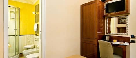 A hotel room with a bed, a desk with a chair, a television mounted on the wall, and a bathroom with a shower and toilet.