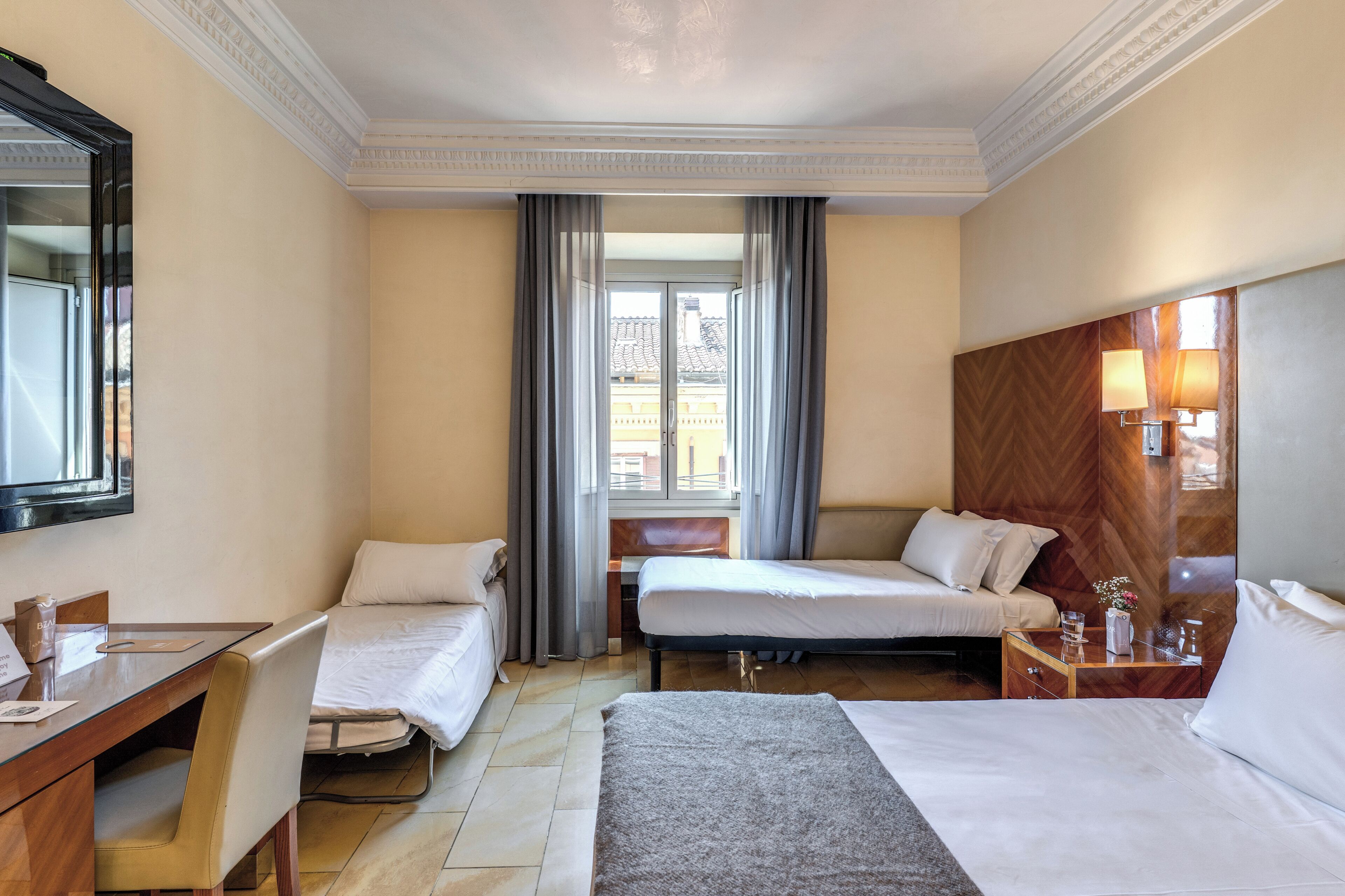 A hotel room with two beds, a desk, a chair, a mirror, and a window with curtains.