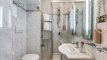 A bathroom with a toilet, a glass-enclosed shower, a sink with a mirror, and a towel rack.