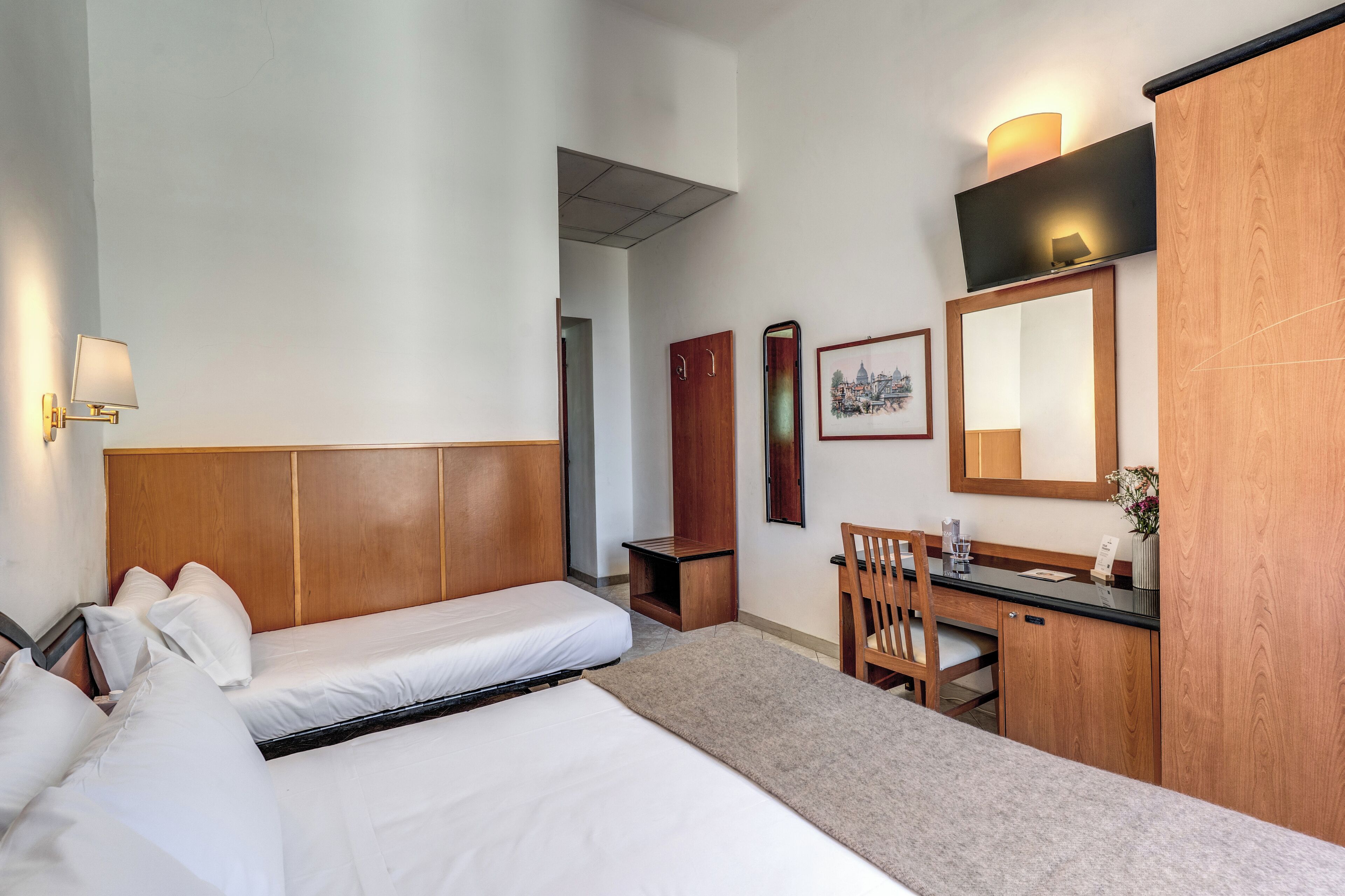 A hotel room with two beds, a desk, a chair, a mirror, and a small cabinet.