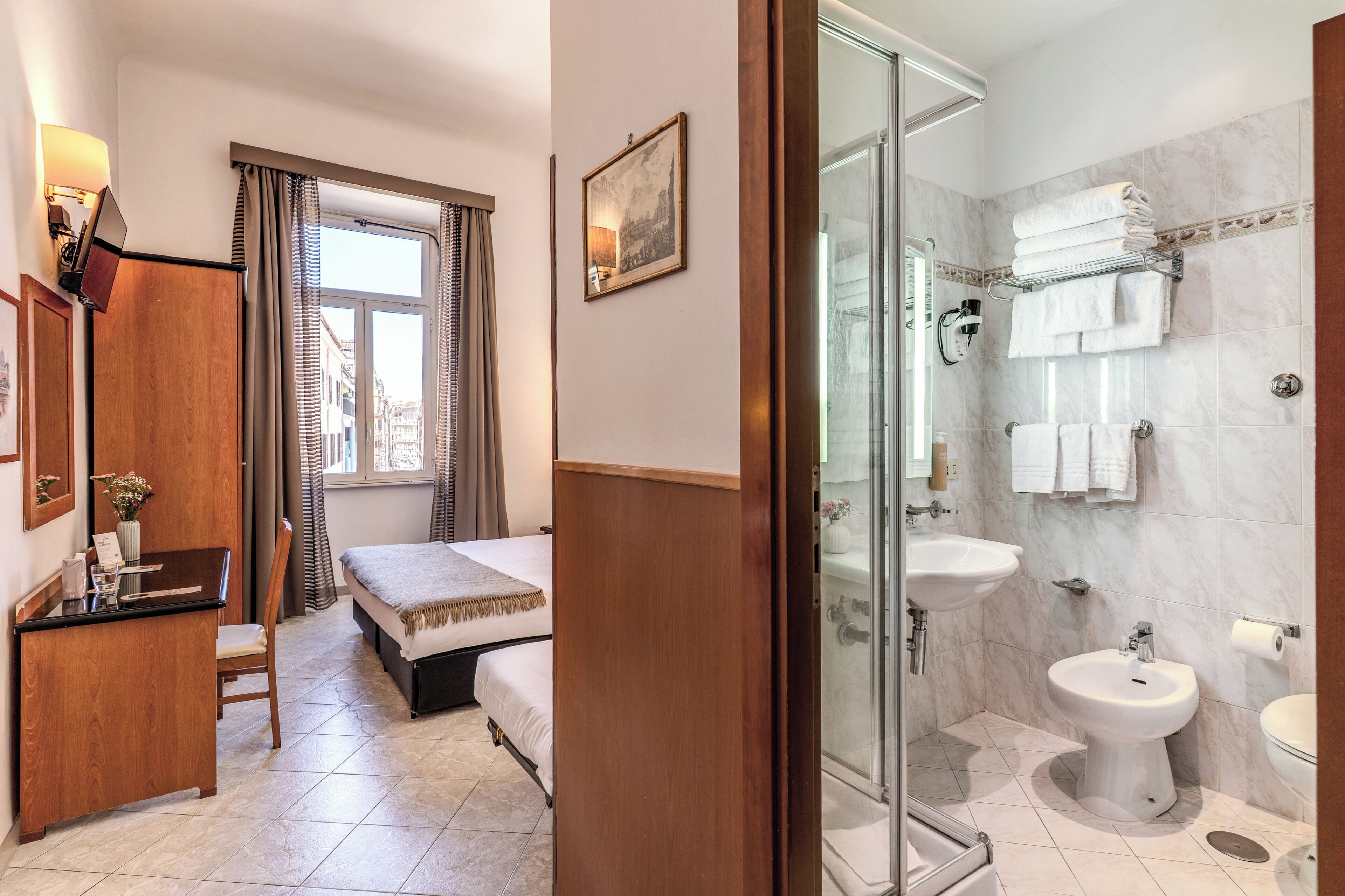 A hotel room with a bed, desk, chair, window with curtains, and a bathroom with a shower, sink, and toilet.