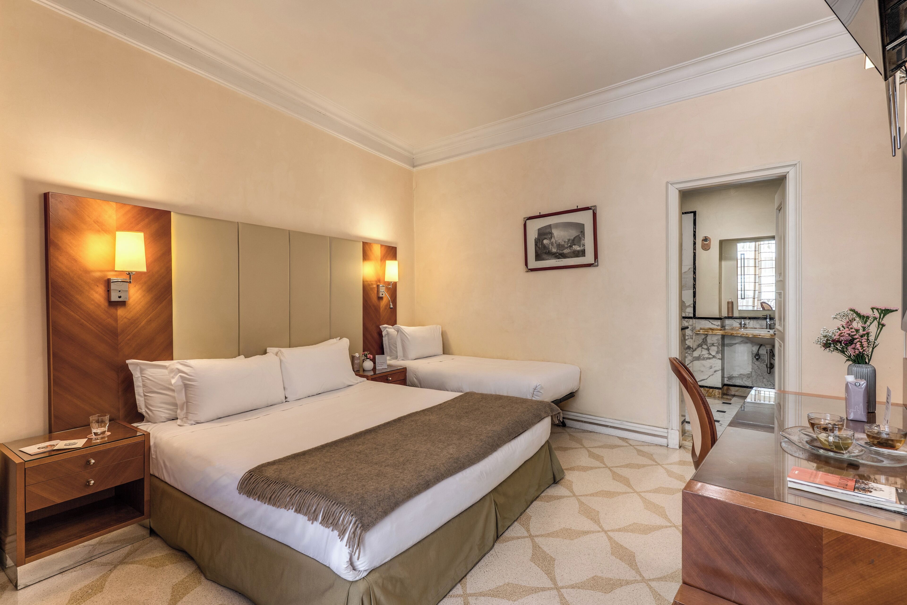 A hotel room with a large bed, bedside tables, a desk with a chair, and a mirror.