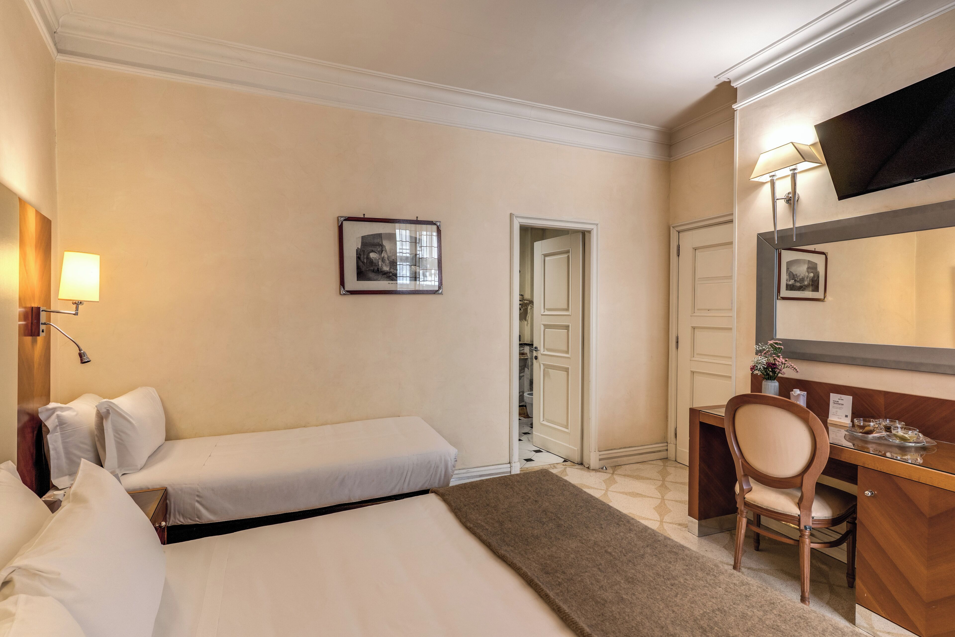 Habitación de hotel con dos camas, un escritorio con silla, televisión y un cuadro en la pared.