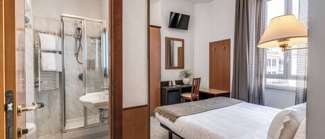 Una camera d'albergo con un letto, una scrivania, una doccia, un lavandino e una televisione.