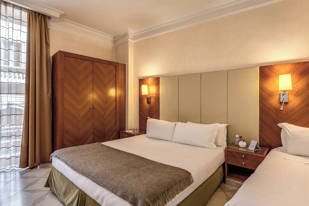 A hotel room with a large bed, a wardrobe, a nightstand, and a mirror.