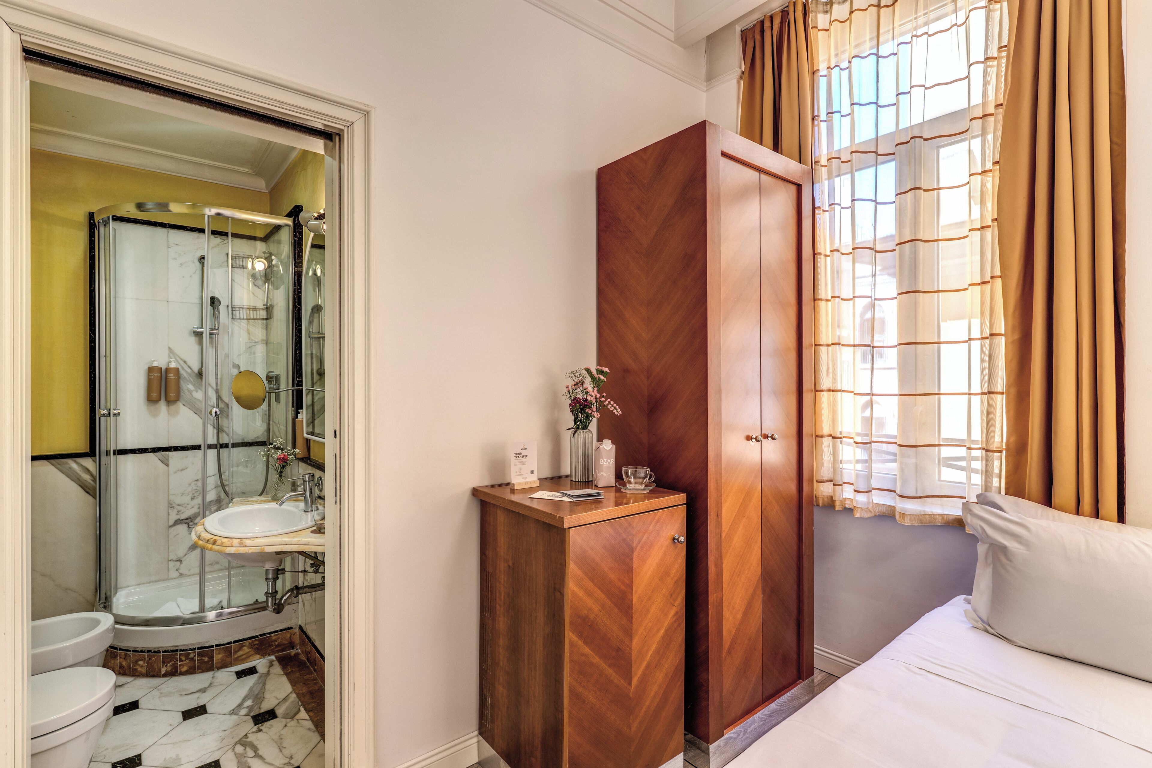 A bathroom with a shower, toilet, and sink, a wooden cabinet, and a bed with a window.