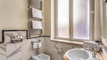 A bathroom with a bidet, a sink, a mirror, and a window with frosted glass.
