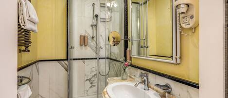 Une salle de bain avec une douche à parois de verre, un lavabo doté d’un plan de travail en marbre et un miroir.