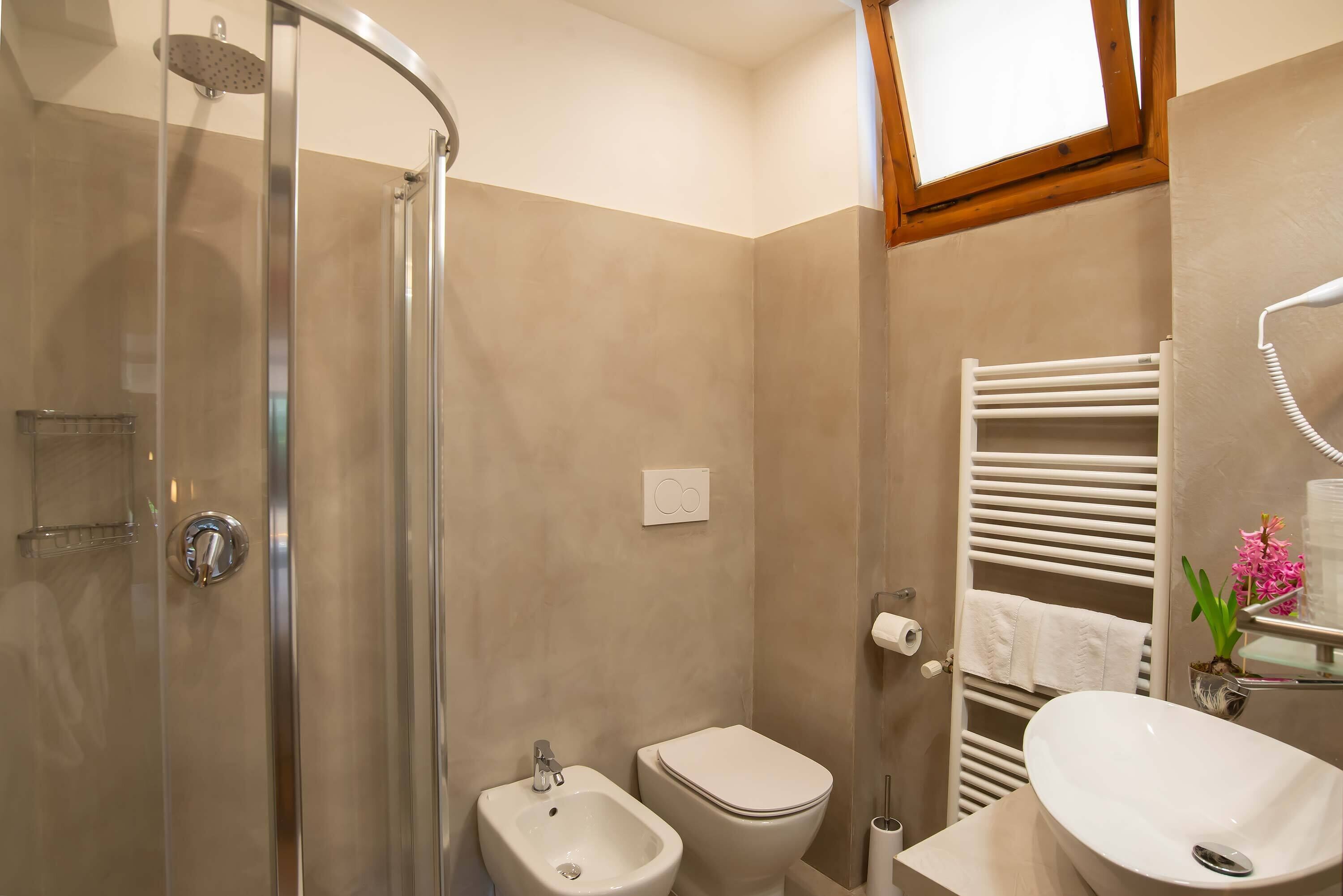 A bathroom with a glass-enclosed shower, a bidet, a toilet, a sink, and a towel rack.